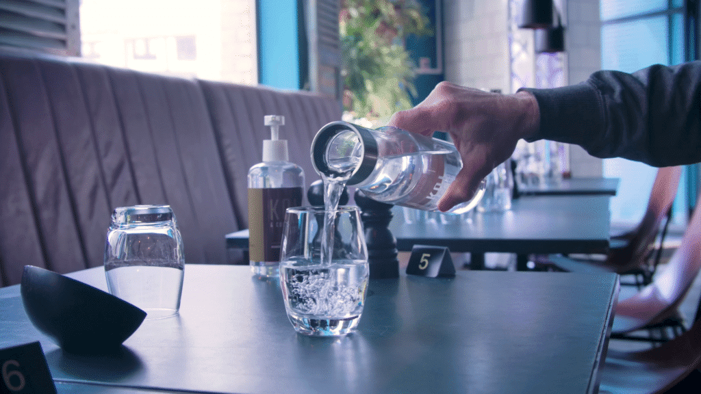 Vatten hälls upp i ett glas ifrån en vattenkaraff med graverad logotyp.