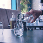 Vatten hälls upp i ett glas ifrån en vattenkaraff med graverad logotyp.