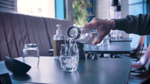 Vatten hälls upp i ett glas ifrån en vattenkaraff med graverad logotyp.