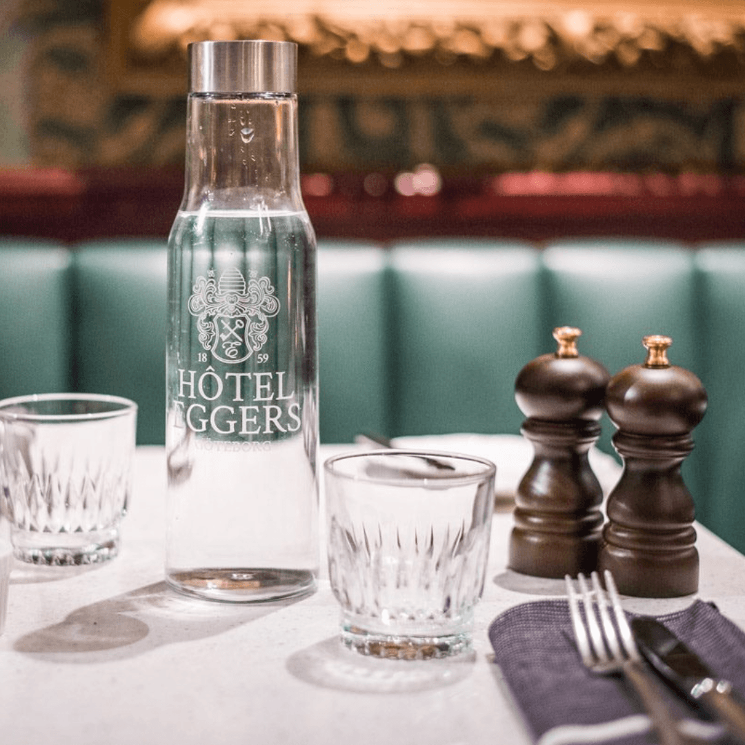 En graverad glaskaraff fylld med vatten på ett dukat bord på en restaurang.