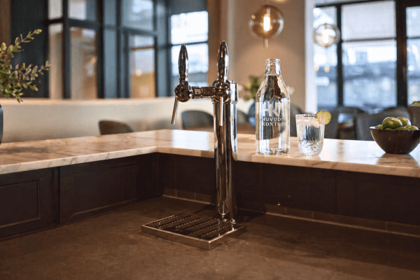 En inbyggd vattenautomat med 2 kranar med kylt och kolsyrat vatten bredvid en graverad karaff.