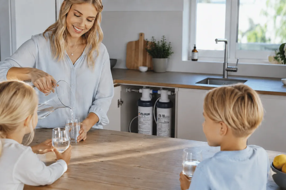Bild av en familjen som dricker vatten, i bakgrunden ser man vattenfilter under diskbänken i köket
